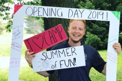 Smiling young man standing in a life sized picture frame that says OPENING DAY 2019