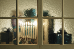 image of a menorah with all 9 candles lit and presents through a window
