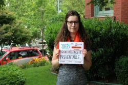 Young woman standing outside holding a sign that says GUN VIOLENCE IS PREVENTABLE with the NFTY and RAC logos