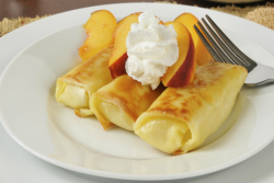 Three blintzes on a plate garnished with peach slices and a dollop of sour cream