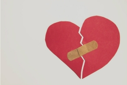 Torn red paper heart held together by a Bandaid against a white background