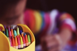Selective focus with a colorful box of crayons in the foreground and a small child coloring in the background