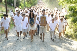 Campers in white being led along a gravel path by two counselors carrying Torah scrolls