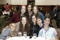 Group of smiling students posing together at a Shabbat dinner table