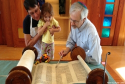 Rabbi, congregant and child look at a Torah scroll