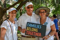Three protesters in white with a "Families Belong Together" sign