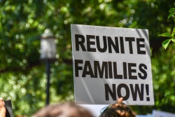 White sign with black text that reads: Reunite Families Now!