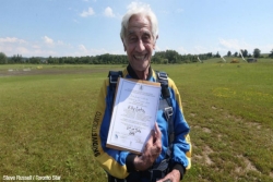 89 year old Elly Gotz wears a skydiving suit and holds a certificate bearing his name after he jumped out of a plane