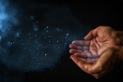Cupped hands emitting sparkles against a dark blue sky 