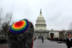 Closeup of a person wearing a rainbow kippah standing in front of the US Capitol building