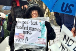 The author smiling while holding a handmade signs that reads Tempest-Tost Huddled Masses Make America Great