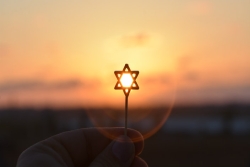 Tiny Star of David charm held up against a sunset 