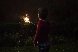 Young boy facing away from the camera while holding a sparkler in the dark