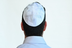 Mans head facing away from the camera wearing a white kippah embroidered with a white Star of David