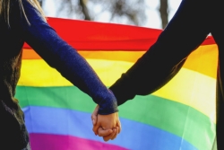 Women holding hands in front of a rainbow flag