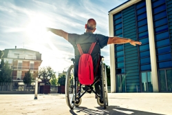 Man in a wheelchair facing a sunrise with his arms up as though celebrating