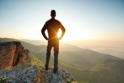 Man facing away from the camera standing on the edge of a cliff at sunset with his hands on his hips