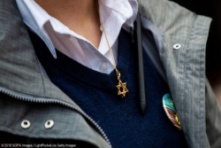 Closeup of a person wearing a Star of David necklace against a blue sweater 