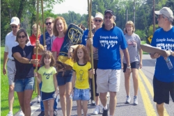 Group of adults and children wearing Temple Israel shirts and carrying a Torah outdoors