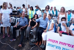 Rabbi Rick Jacobs seated at a Women Wage Peace rally event taking selfies with other attendees