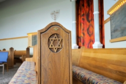 Side view of empty synagogue pews zoomed in on wooden carving of Star of David design at the ends of the pews