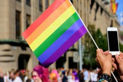 Person hold Pride flag and using cell phone to photograph a Pride parade