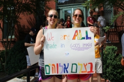 Two young women holding a rainbow sign that reads WERE ALL CREATED IN GODS IMAGE