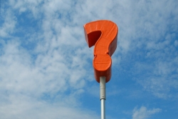 Red question mark on a pole against a blue sky background 