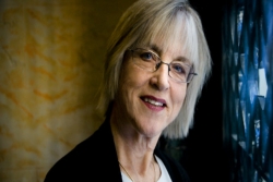 Photo of the late Rabbi Rachel Cowan with blond hair and bangs and her head cocked to the right side smiling at the camera