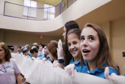 YouTube screenshot of girls in school uniforms smiling while holding an open Torah scroll