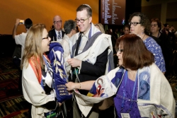 Four smiling worshipers gather around a Torah
