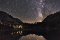 Dark night full of stars above a campfire near a lake
