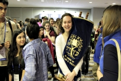 Smiling teen girl holding a Torah in a crowd of teens