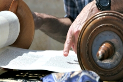 Closeup of a mans hand reading Torah on a table outdoors
