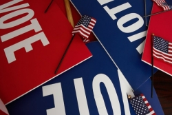 A pile of voter signs in red white and blue with small American flags sprinkled atop them 