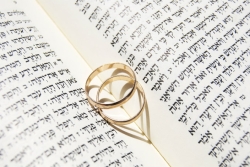 Two gold wedding band lying atop the spine of an open book with a heart shaped shadowed on the pages beneath them