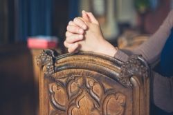 Closeup of a woman's hands resting on a wooden pew 
