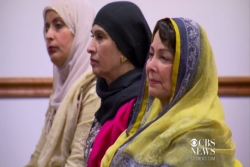 Three middleaged women in hijab sitting in mosque pews during a service