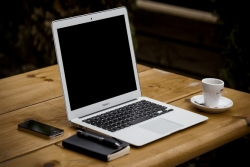 Laptop on a wooden table surrounded by a coffee cup notebook and phone