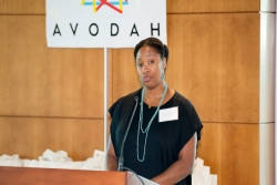 The author stands behind a wooden podium in front of an AVODAH sign