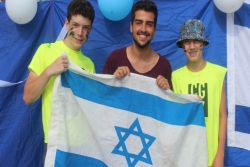 Three smiling male teens holding an Israeli flags