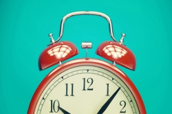 Old fashioned red alarm clock with white face and bells on top against a turquoise background