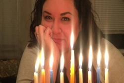 Amanda Ryan rests her chin her her hand and smiles behind a fully lit menorah
