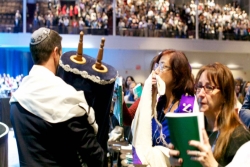 Man walking the Torah through aisles of people at the Biennial as they kiss the scroll