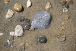 Assorted rocks and stones on wet sand; largest one says Blessings