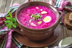 Bowl of bright pink borscht garnished with hard-boiled egg and greens