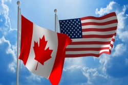 Canadian and American flags flying; blue sky and white clouds in the background
