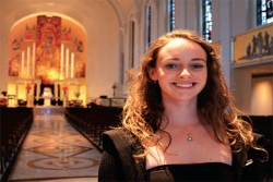 Young Woman Stands in Church with Altar Lit Up in Background
