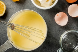 Overhead view of hollandaise sauce and whisk in a pot