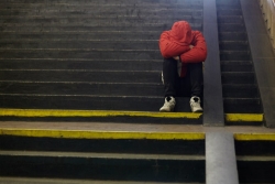 Young man in sweats, head down, sitting on the bottom step of a flight of stairs